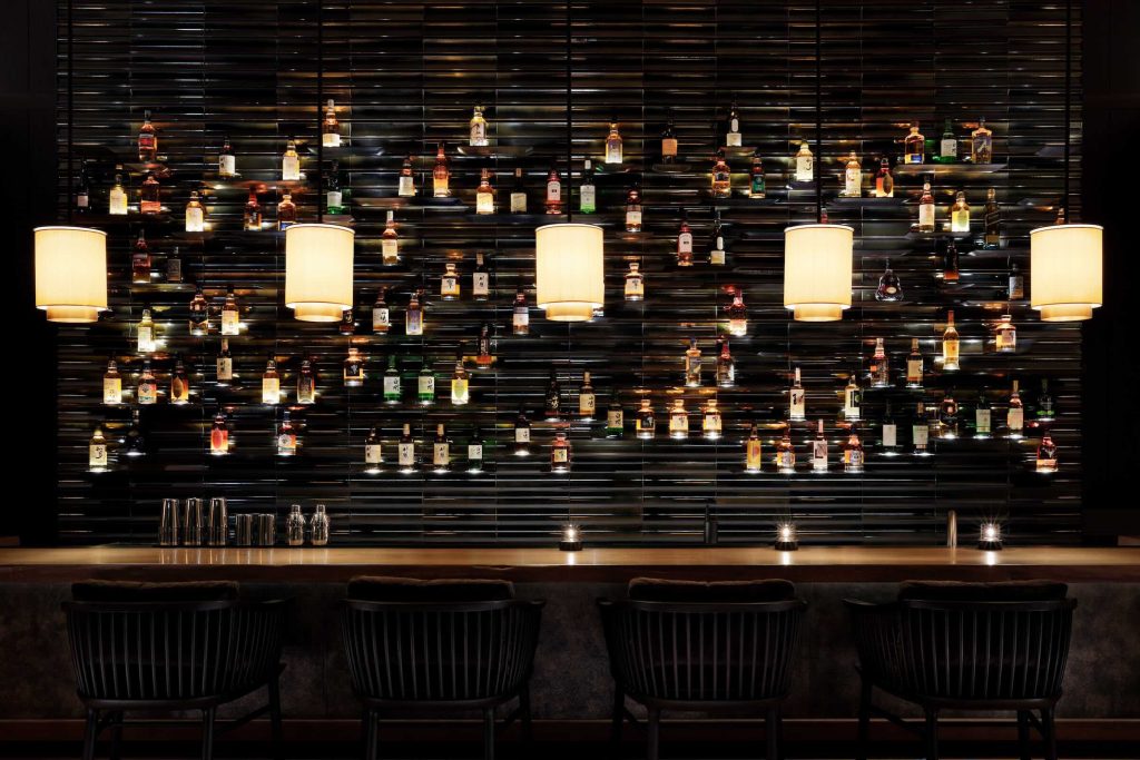A cosy bar setting with a wall filled with Japanese whisky bottles and illuminated by lights.