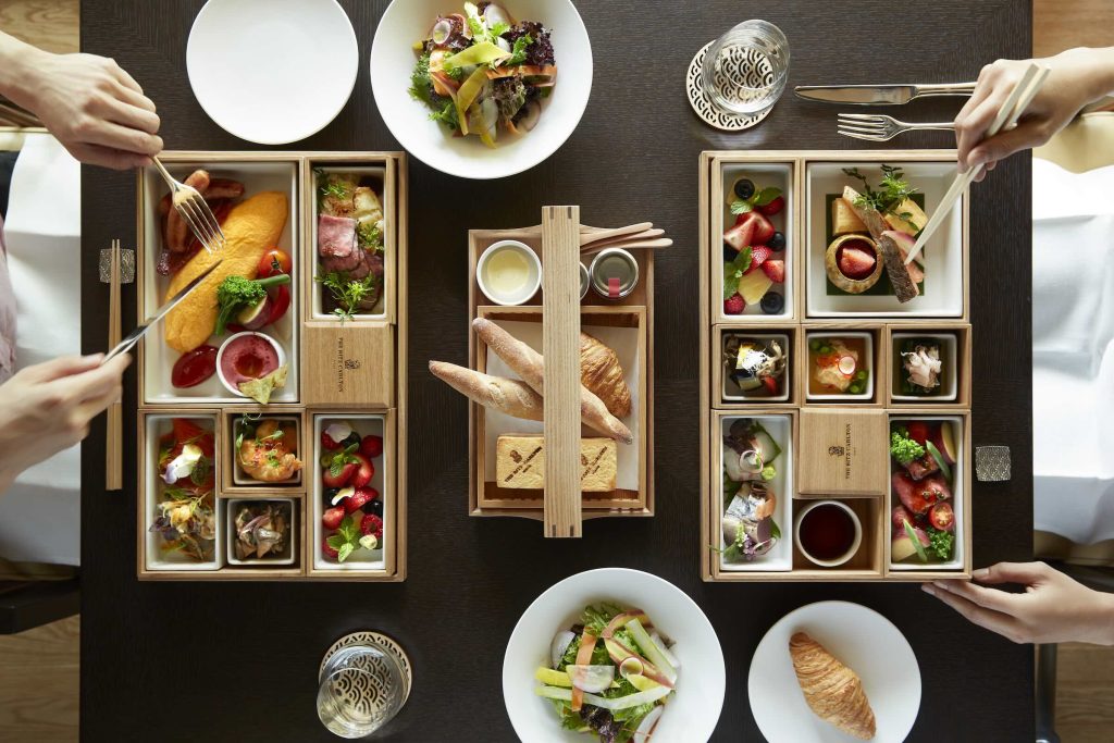 Large wooden bento boxes with an assortment of different breakfast foods, pastries, and salad.