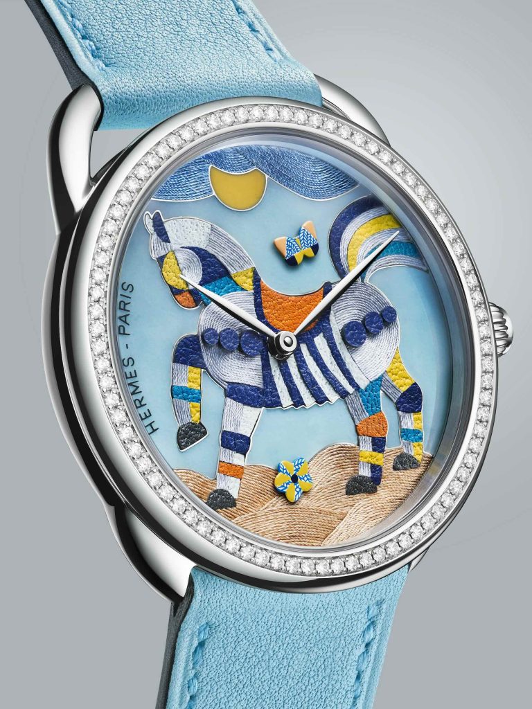 Close-up of the Arceau Mon Premier Galop by Hermès, featuring a textured dial made of silk threads, leather panels, and enamel painting, showing a galloping horse.