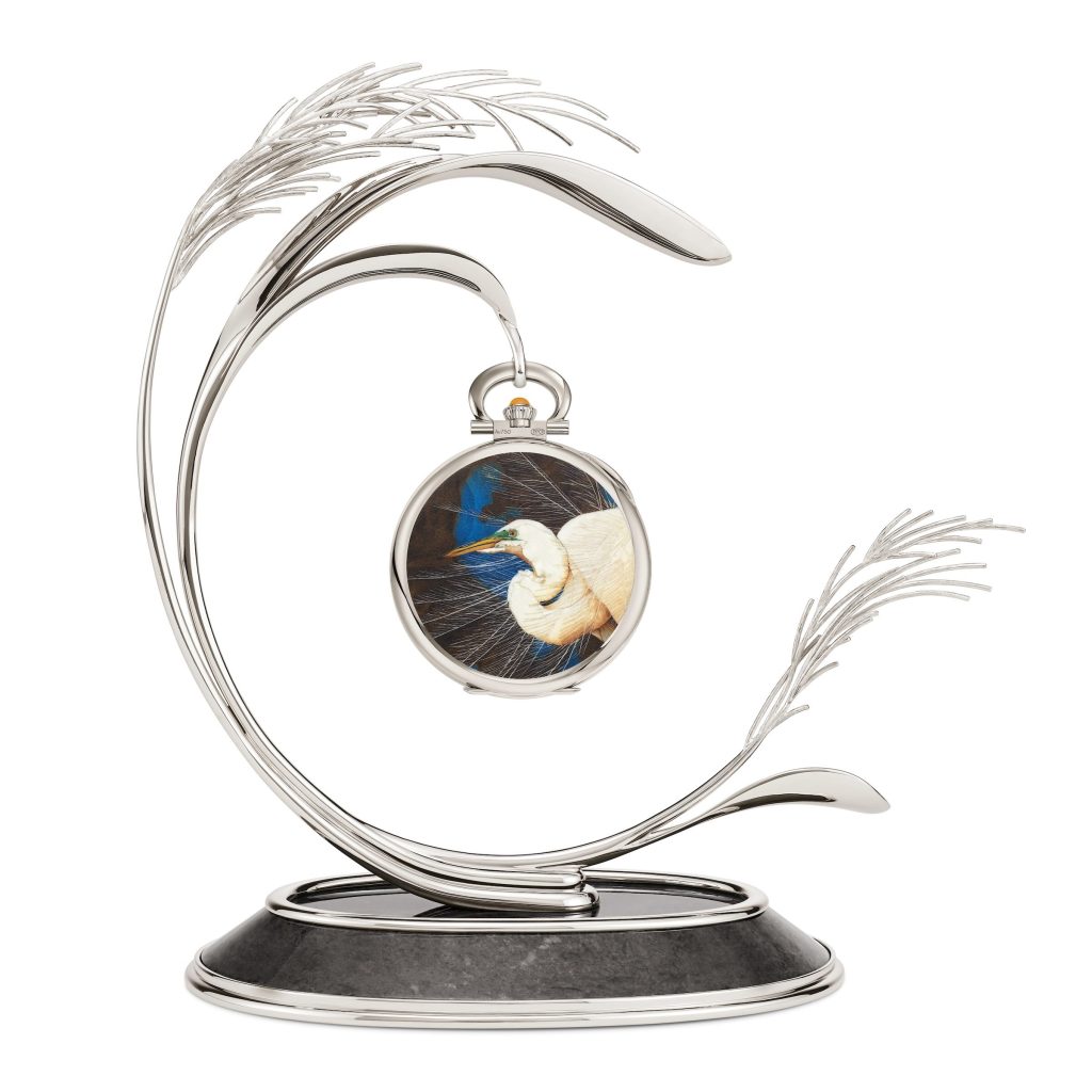 White-gold pocket watch featuring a white egret motif hangs on a handcrafted stand with a curved feather design.