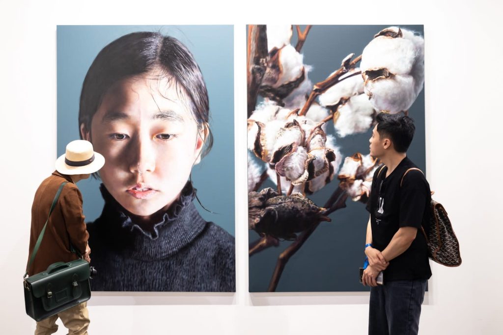 Two visitors viewing hyperrealistic artworks at Art Basel Hong Kong.
