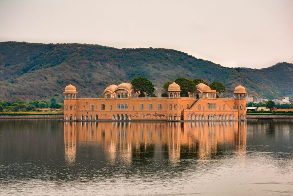 A large brown palace sitting atop a lake, against a background of mountains.